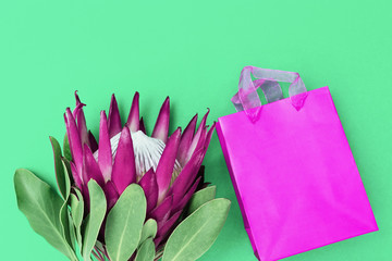 Exotic big flower protea with purple petals and present in decorated paper box on bright background. Holiday concept witn natural flower. Top view and copy space. Minimal composition.