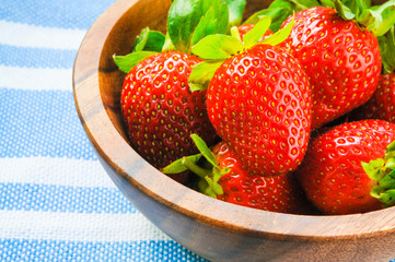 Fresh strawberry in wooden bowl on white blue fabric