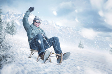 Happy man sledding down a slope in winter - obrazy, fototapety, plakaty
