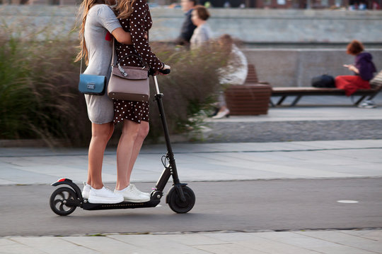 in the city summer park, two girls ride on the same scooter
