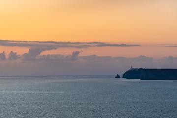 Obraz premium The landscape is warm colours. A Lighthouse on a rock against the backdrop of a sunset sky.