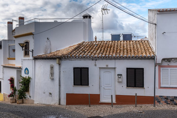Fototapeta na wymiar Traditional Portugal street with house facade, what has an old door on the bright white wall and red tiled roof.