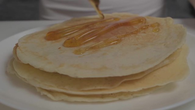 Organic honey flows on thin pancakes. Girl puts honey on pancakes for Breakfast. Slow motion. Close up.