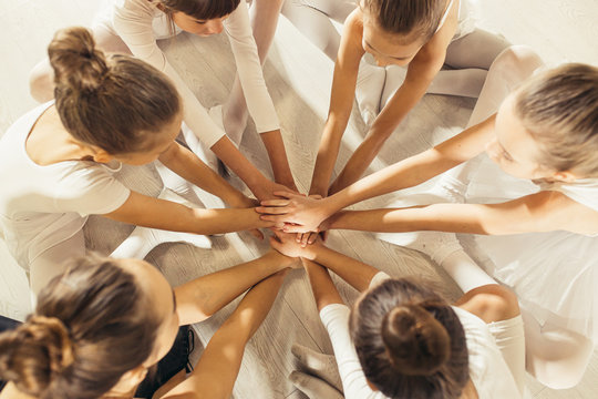 top view on team, group of friendly little ballerinas joining hands together sitting in circle, ballet concept