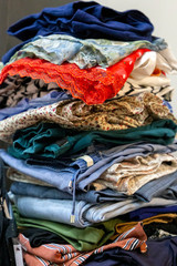 A tall stack of folded women's clothing. A pile of clothes for washing, ironing, donations. The concept of organization of life. Closeup view.