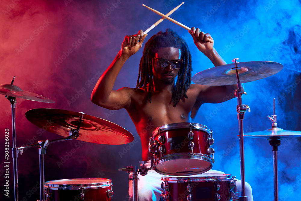 Wall mural awesome black man with naked skin playing on drums, isolated over neon smoky background