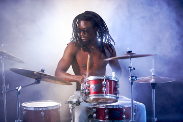 good-looking artistic african black male drummer enjoying playing drums over white smoky background