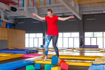 Fototapeta na wymiar Fitness, fun, leisure and sport activity concept - Young happy woman jumping on a trampoline indoors