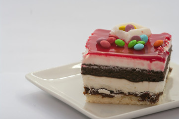 closeuo of a Big piece of cake in a white plate with multi-colored candies on it