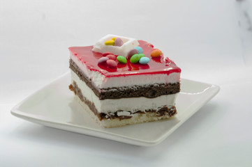 closeuo of a Big piece of cake in a white plate with multi-colored candies on it