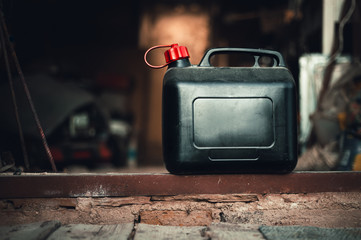 Old and dirty plastic black gas can  fuel container standing on ground from bricks with garage on background. Black petrol can with a lot of tools in storage (workshop). - obrazy, fototapety, plakaty