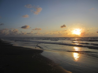 Fototapeta na wymiar Sunrise is reflected in the water and sand on Packery Channel Jetty beach, Padre Island, Texas
