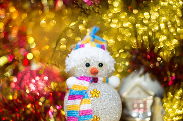 Lovely Christmas composition - a toy snowman against the background of Christmas toys and bright bokeh.