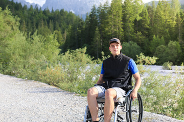 Happy young man in wheelchair outside in nature on a sunny summer day