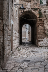Fototapeta na wymiar Narrow street in the old town, stone walls, arched passage, lantern. Monopoli, Italy.