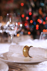A white cloth napkin rests on a white plate and is secured with a vintage ring. Stylish design of the table for the New year. Christmas tree out of focus. The concept of bokeh.