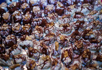 Close up of many isolated fresh homemade white and brown chocolate pralines filled with dates fruits, decorated with walnuts and  spread out on tray with Aluminium foil to dry