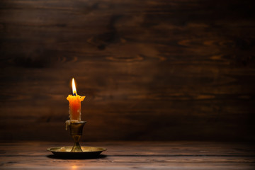 burning old candle with vintage brass candlestick on wooden background in minimalist room interior with copy space