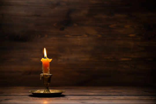 burning old candle with vintage brass candlestick on wooden background in minimalist room interior with copy space