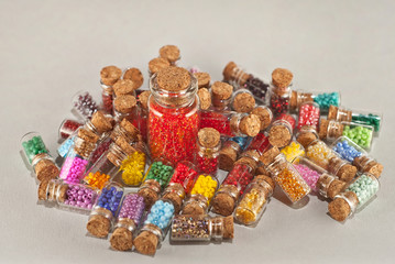 Red, yellow, blue, green, purple, pink and orange beads in glass jars on a gray background. Beads in a transparent container with a wooden cork. The concept of orderliness, balance and chaos.