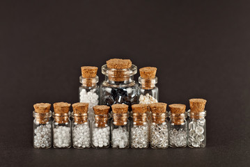 White, beige, yellow and gray beads in glass jars on black background. Beads in a transparent container with a wooden cork. The concept of orderliness, balance and chaos.