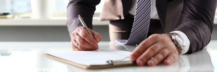 Male arm in suit and tie fill form clipped to pad © H_Ko