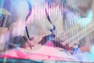 A woman hands writing information about stock market in notepad. Forex chart holograms in front. Concept of research.