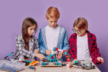 Portrait of caucasian little children assembling robots - group of happy kids or students with...