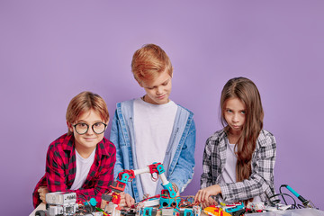 portrait of clever children assembling robots on table, teamwork, children involved in engineering, robotics