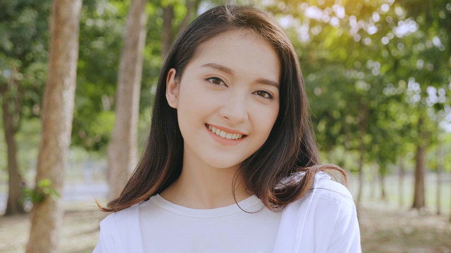 Asian woman close up face Beautiful, smiling happily, standing in a park with trees. The background is bright green bokeh. Relaxation helps to relax the body. And has a younger face.