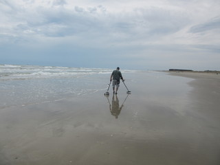 A man hunts for treasure with a metal detector on Packery Channel Jetty beach, Padre Island, Texas