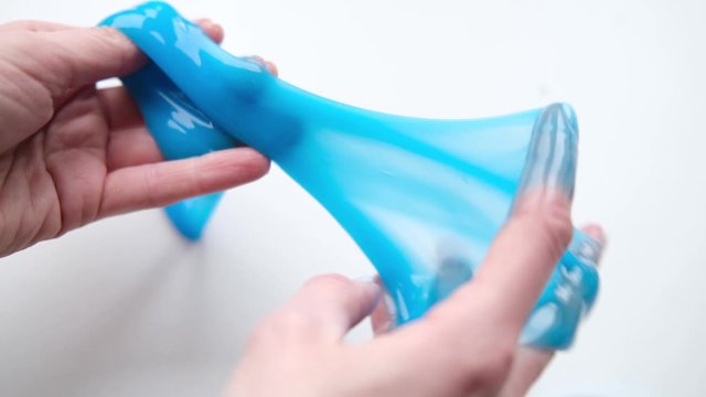 Girl stretching blue slime to the sides. Woman hands playing slime toy. Making slime on white. Trendy liquid toy sticks to hands and fingers. 4k footage.