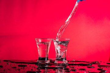 two falling glasses with vodka in motion are frozen with a spray and a splash