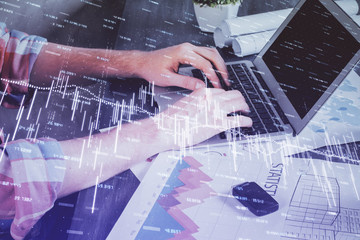 Double exposure of stock graph with businessman typing on computer in office on background. Concept of hard work.