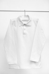 White polo shirt with long sleeves for a toddler boy hanging on a shoulders (hanger) isolated on white background