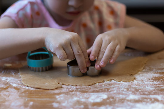 children's hands cut out a heart-shaped cookie on a rolled raw ginger dough