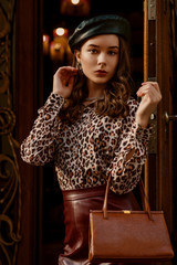 Outdoor fashion portrait of young elegant woman wearing black beret, leopard print blouse, faux...