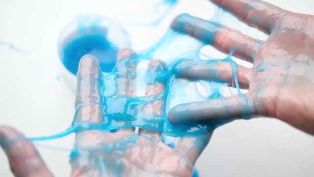 Girl stretching blue slime to the sides. Woman hands playing slime toy. Making slime on white. Trendy liquid toy sticks to hands and fingers. 4k footage.