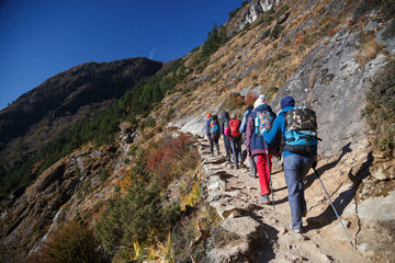 Travellers follow a narrow path on a mountainside. Bright sunny day. Nepal. 