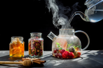 Pouring tea in cup of hot tea in of healthy herbal tea with mint, orange ,grape, dried rose and camomile flowers in tea pot.hot food concept