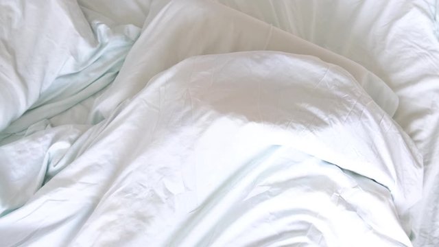 A little blond boy lies in bed and smiles, is having fun, hiding under the covers and peeping from under him in the early morning. Time to wake up.
