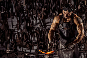 Plakat strong muscular brutal confident blacksmith man shaping red hot metal with hammer isolated in workshop, wearing leather apron, dark space