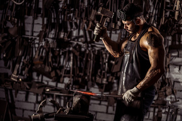 Obraz na płótnie Canvas muscular man work at workshop using hammer, wearing leather uniform and having strong body