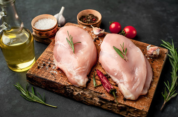 Raw chicken fillet on a cutting board with rosemary, spices, tomatoes and pepper on a stone background