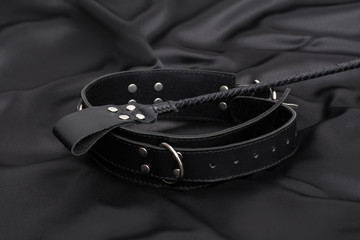 Stack for bdsm games and leather collar on black silk background.