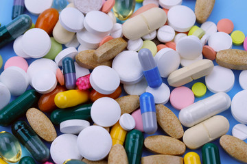 A pile of bright medicine pills on a blue background. Cropped shot, horizontal, top view. The concept of medicine and health. Opioid Painkiller Crisis and Addiction Concept