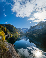 Fototapeta na wymiar Autumn Alps mountain lake with clouds reflections. Gosauseen or Vorderer Gosausee lake, Upper Austria. Dachstein summit and glacier in far.