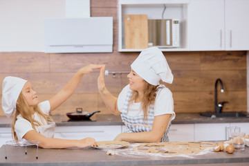 playful cheerful mother and little girl look at each other and play in kitchen, while making dough