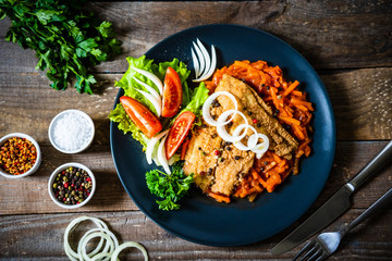 Fish dish - fried fish fillet on vegetable sauce on wooden table