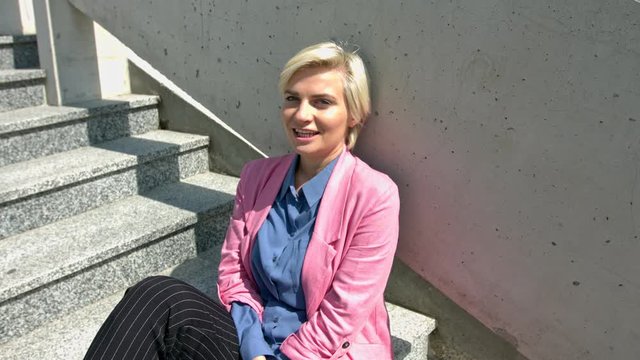 A Beautiful Woman Wearing Pink Blazer Sitting On The Stair Smiling While Looking At The Camera  - Close Up Shot 